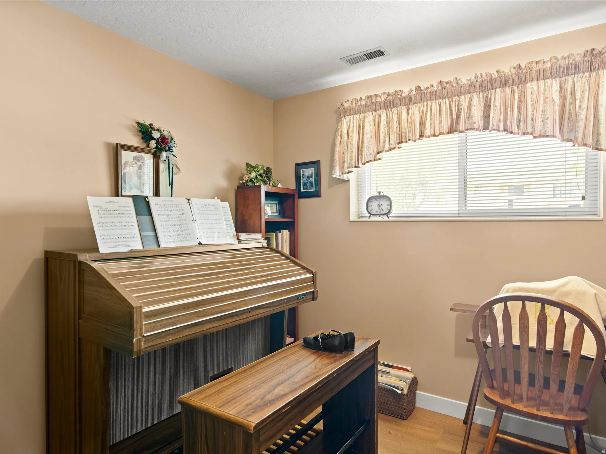 Window with blinds, warm-toned walls, and wood-finish flooring