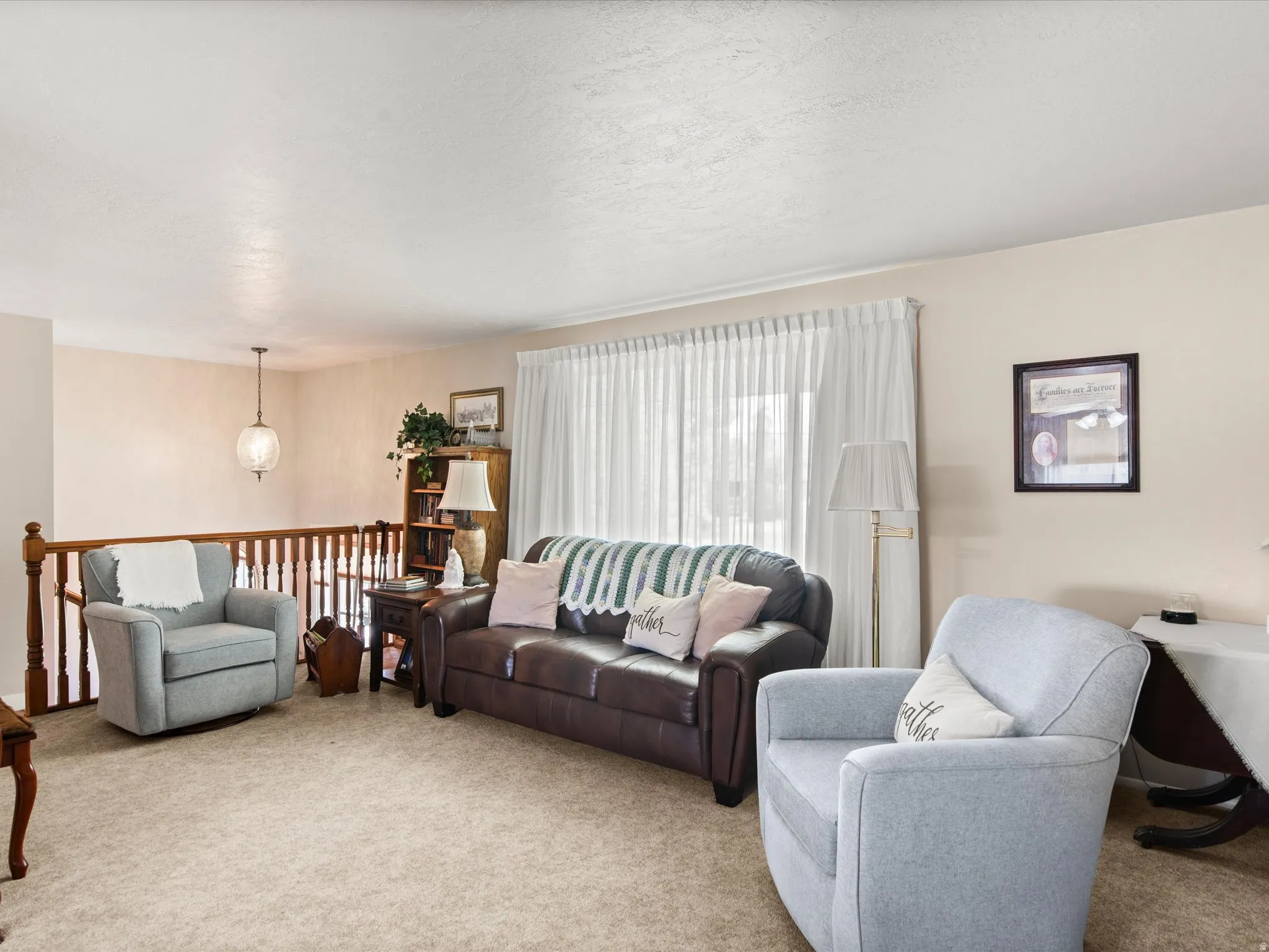 Carpeted living area featuring a wooden railing, white window coverings, and a ceiling-mounted light fixture