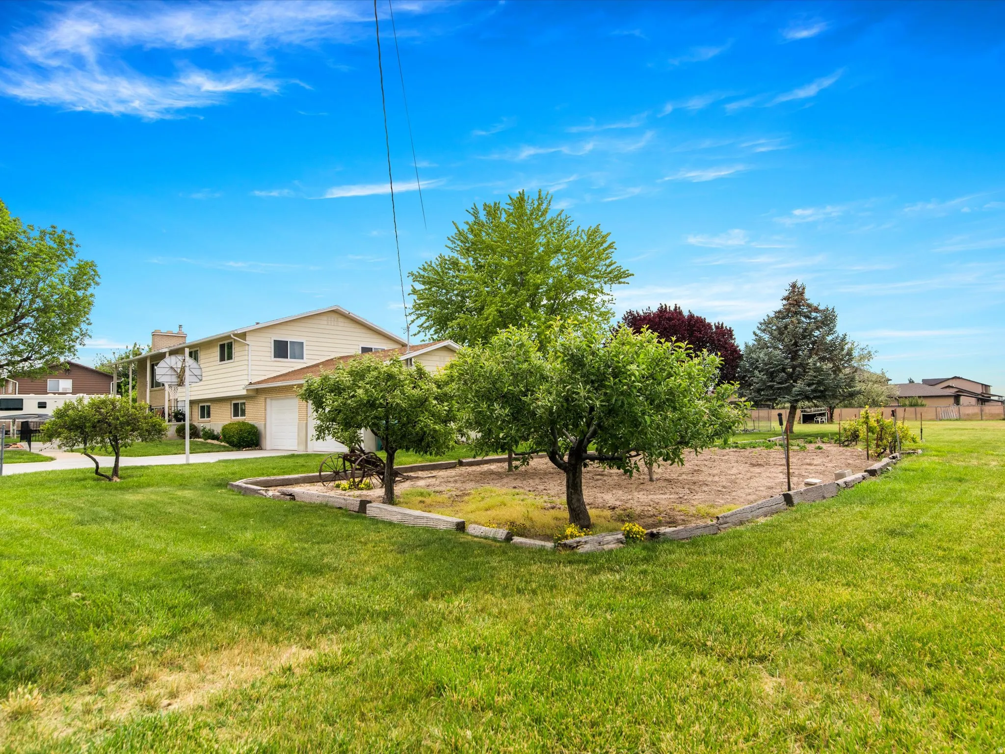 Expansive lawn area featuring a raised garden bed with mature trees, established perimeter fencing, and a basketball hoop