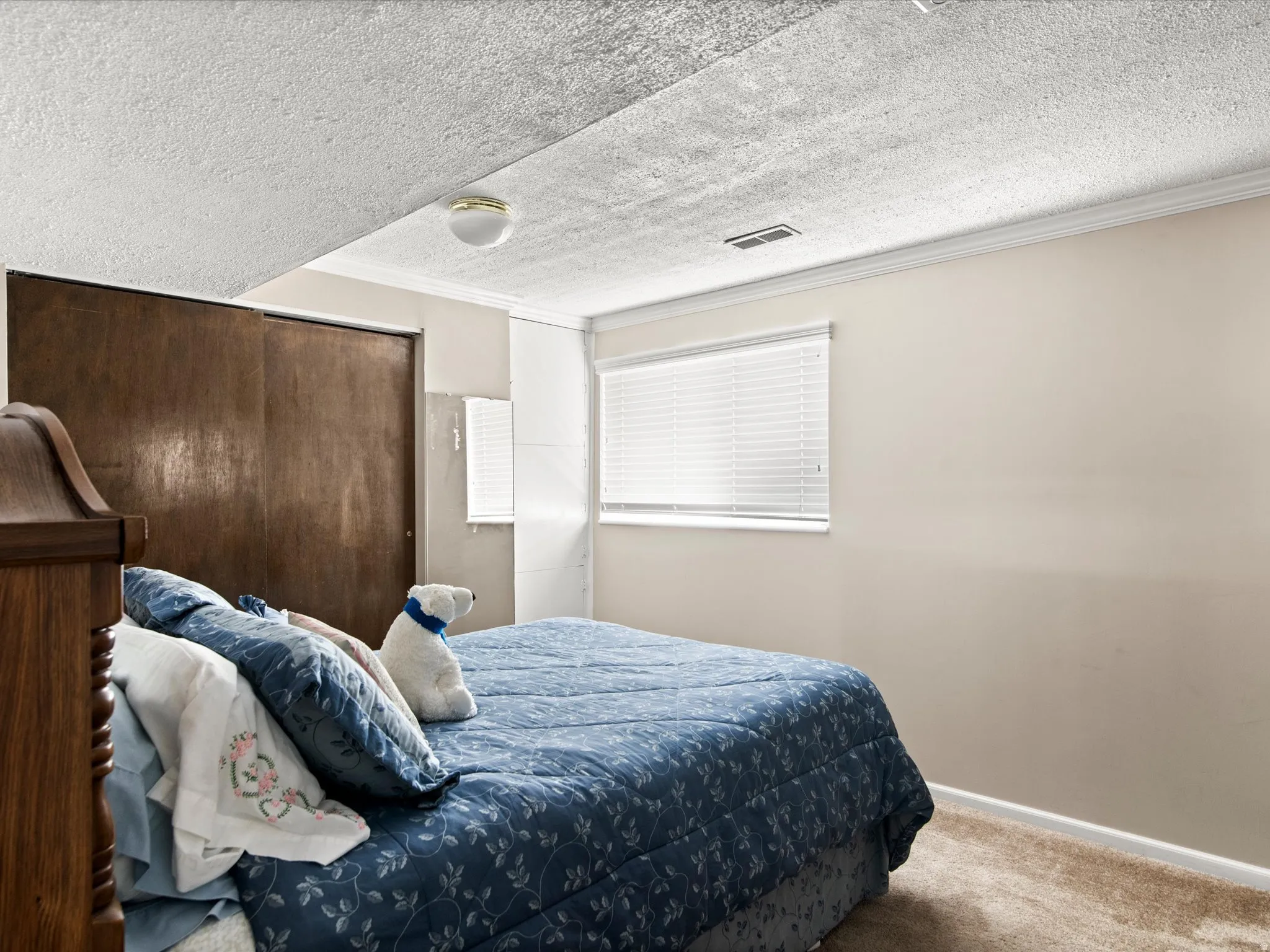 Spacious room featuring neutral carpeting, a single window with blinds, and a built-in closet with sliding wood-panel doors