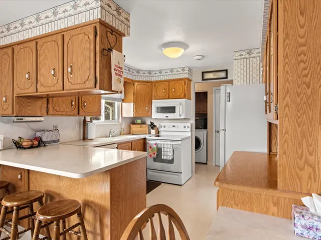Kitchen featuring light wood cabinetry, white countertops, built-in microwave, white appliances, and a window above the sink