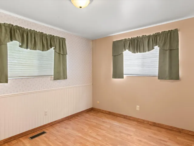 Room featuring wood-finish flooring, two windows with blinds, and a ceiling-mounted light fixture