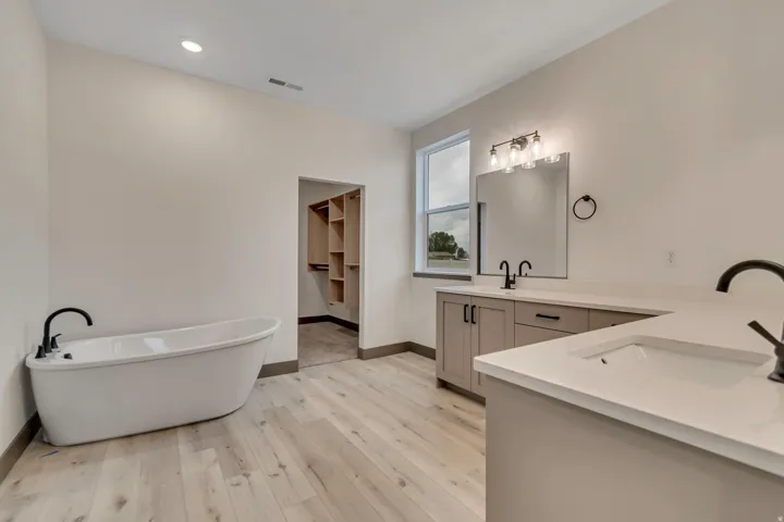 Full bathroom with double vanity, a freestanding bath, light wood-type flooring, a walk in closet, and recessed lighting