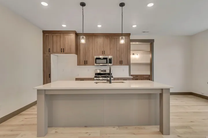 Kitchen with decorative light fixtures, light wood-type flooring, stainless steel appliances, wood finish cabinetry, and light stone countertops