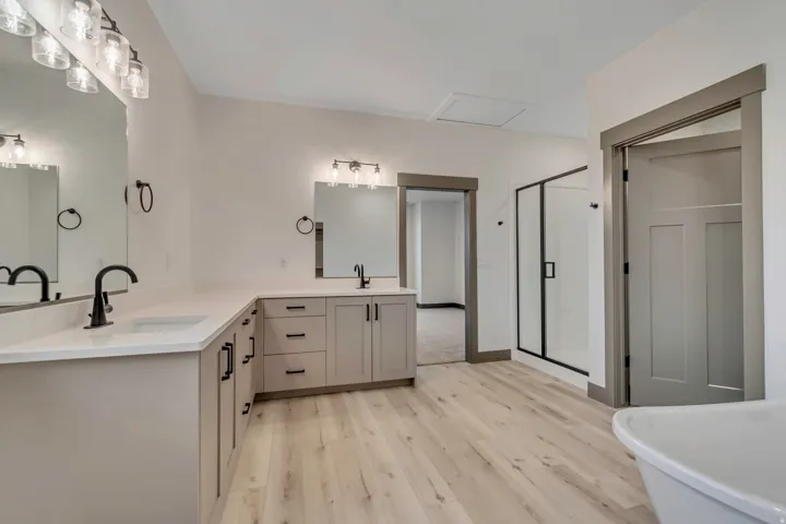 Bathroom with double vanity, a shower stall, light wood-style flooring, and a soaking tub