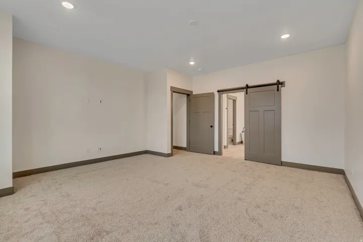 Unfurnished bedroom featuring a barn door, light carpet, recessed lighting, and ensuite bath