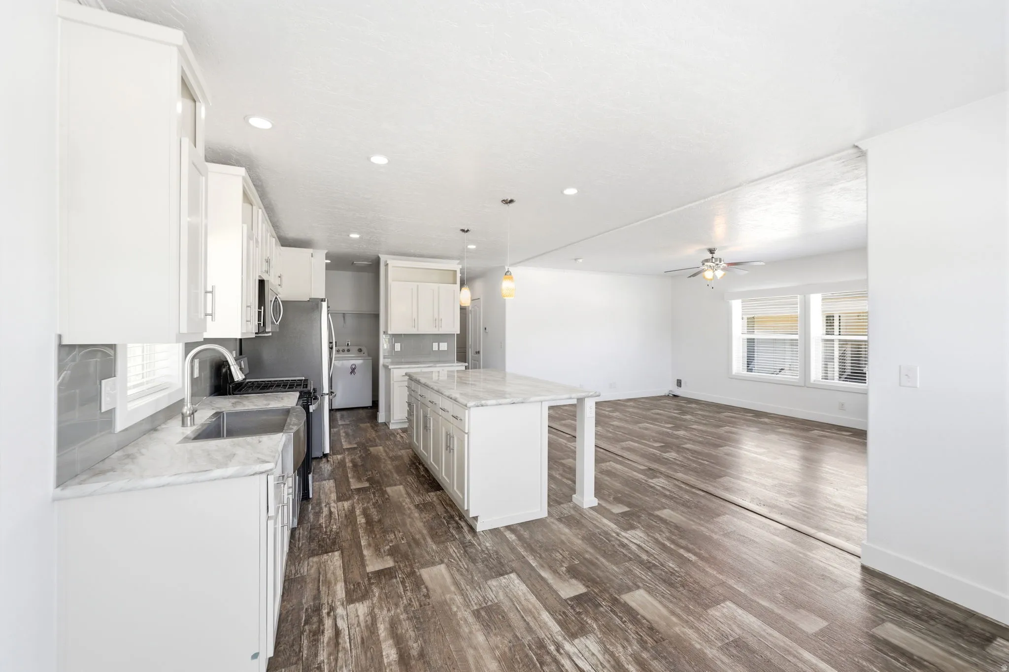 Open-concept kitchen and living area featuring wood-finish flooring, white cabinetry, a kitchen island with a light-toned countertop, stainless steel appliances, and recessed lighting