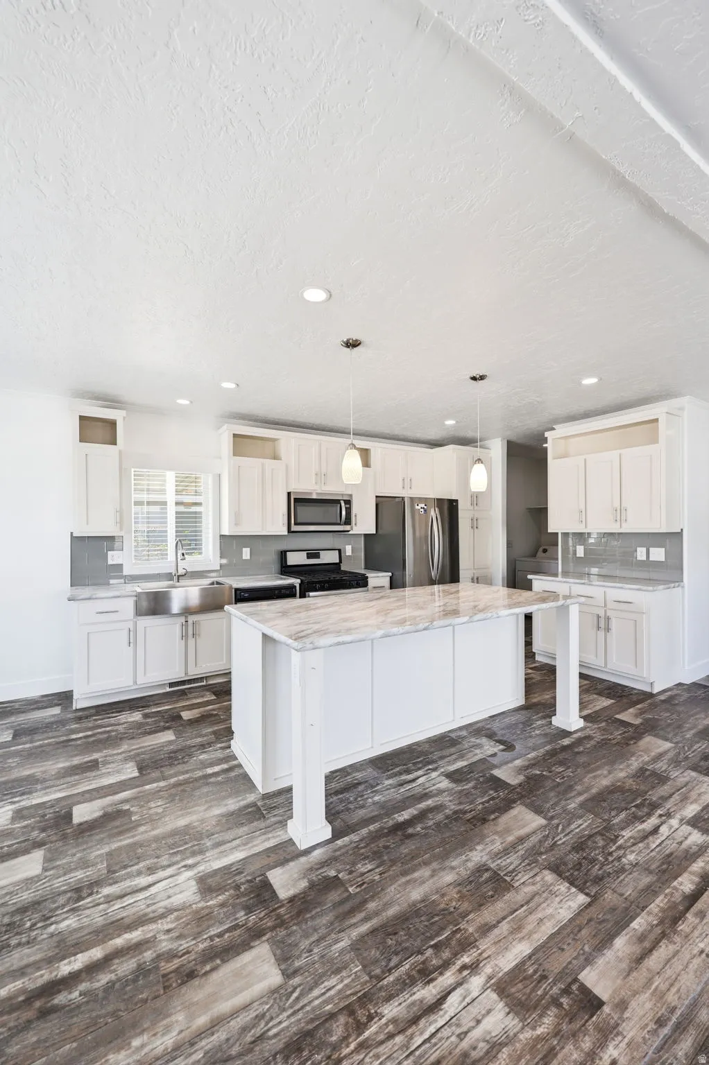 Spacious kitchen featuring an expansive center island with a stone-look countertop, ample white cabinetry, stainless steel appliances, and wood-finish flooring