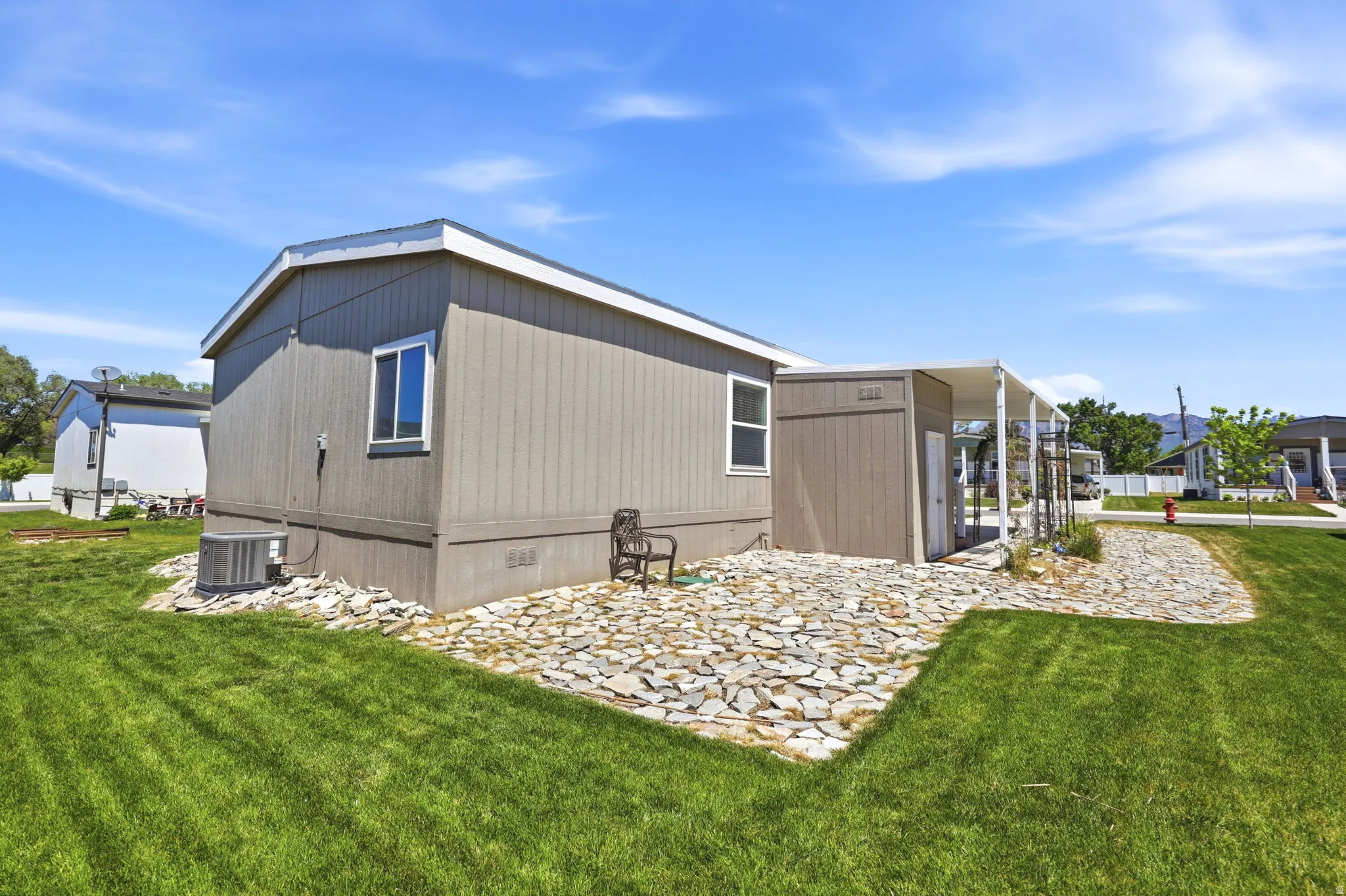 Exterior featuring gray vertical panel siding, white trim, a covered porch entry, and a flagstone patio area