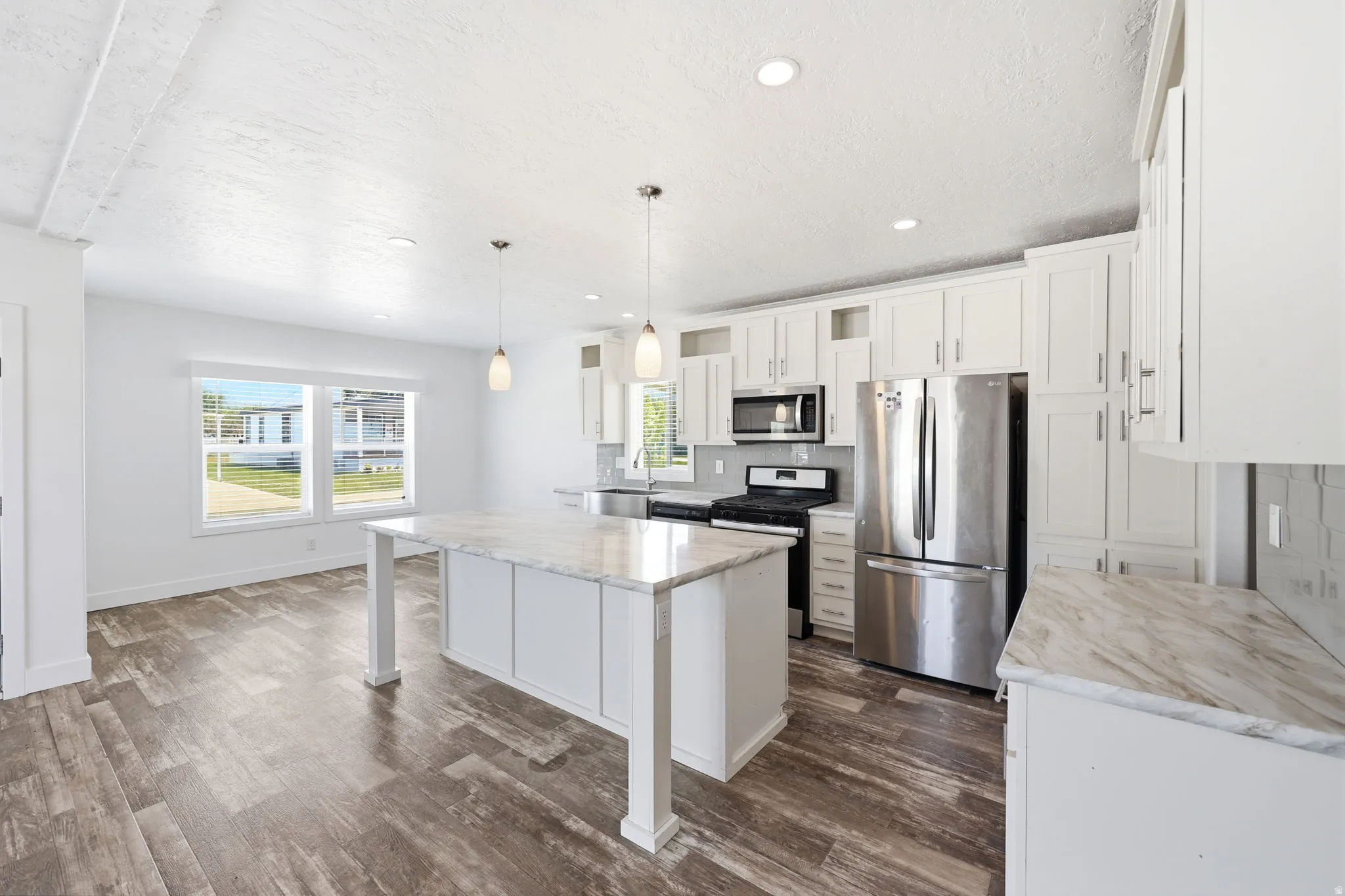 Contemporary kitchen featuring a large central island with a light-toned countertop, white cabinetry with silver-tone hardware, stainless steel appliances, and pendant lighting