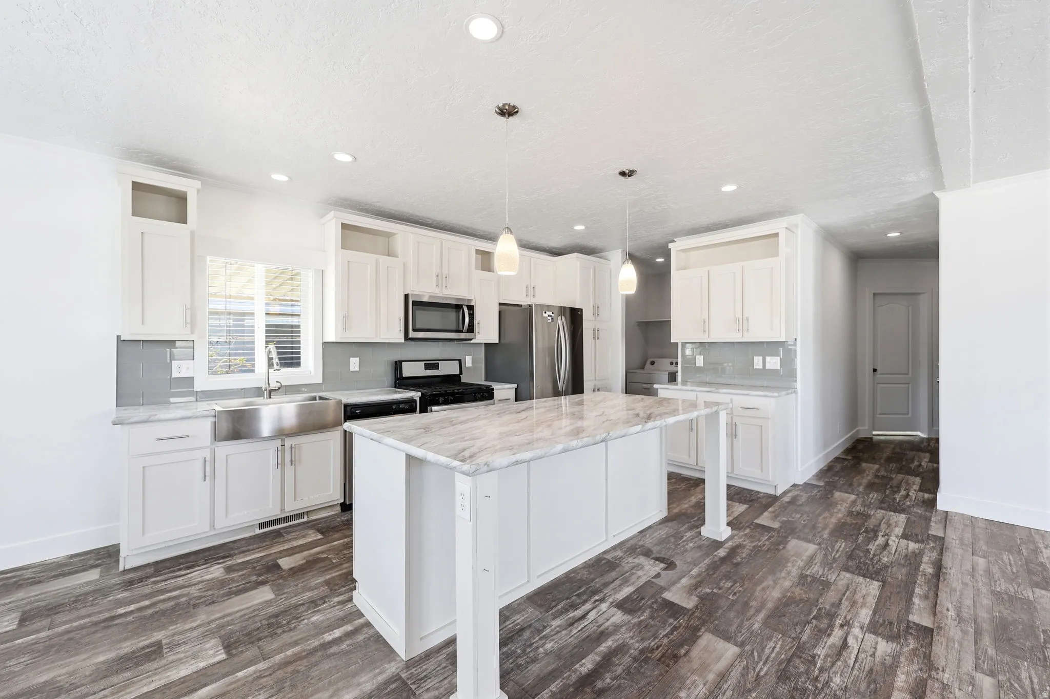 Bright kitchen featuring a central island with a stone-look countertop, recessed lighting, pendant lighting, stainless steel appliances, and wood-finish flooring