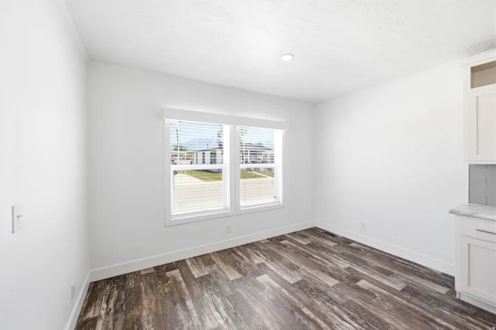 Bright room featuring two windows with blinds, wood-finish flooring, white walls, and a built-in cabinet with a marble-patterned countertop