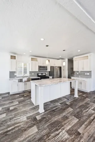 Spacious kitchen featuring an expansive center island with a stone-look countertop, ample white cabinetry, stainless steel appliances, and wood-finish flooring