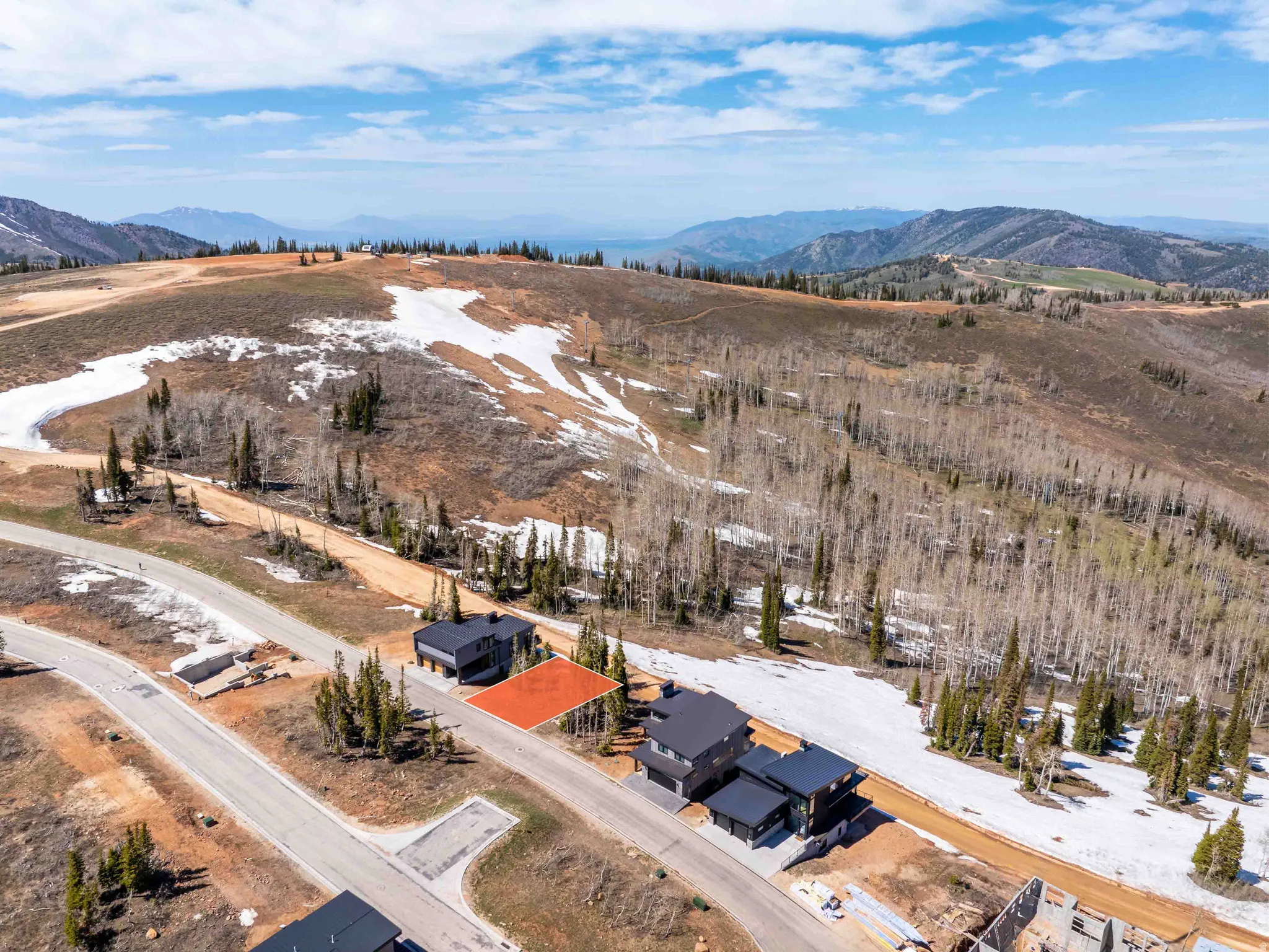 Mountainous terrain with natural snow patches, visible road infrastructure, and surrounding residential structures