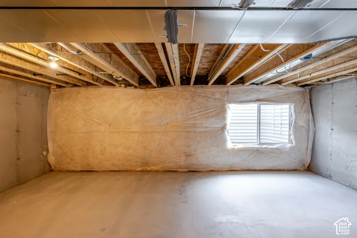Unfinished space featuring exposed wood ceiling joists, concrete foundation walls, a single egress window, and concrete flooring