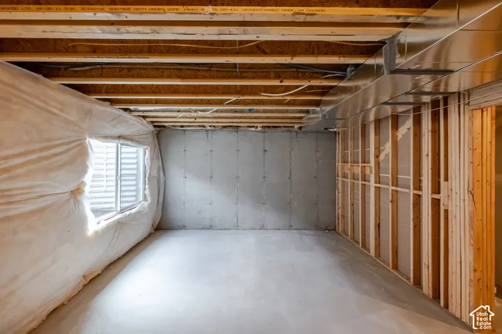 Unfinished interior space featuring exposed wood joists, concrete foundation walls, concrete flooring, metal ductwork, and an installed window