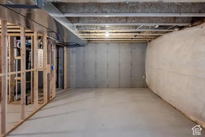 Unfinished basement area featuring concrete foundation walls, concrete floor, exposed wooden framing, and exposed ceiling joists with metallic ductwork