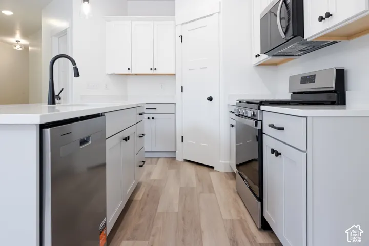 Kitchen featuring white shaker-style cabinetry, quartz countertops, stainless steel appliances, wood-finish flooring, and matte black hardware