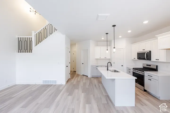 Kitchen featuring white shaker-style cabinetry, quartz countertops, a central island with a pull-down faucet, and wood-finish flooring