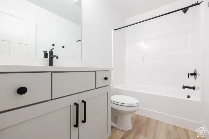 Contemporary bathroom featuring a gray vanity with dual drawers and black hardware, white quartz countertop, matte black faucet and fixtures, white subway tile surround, and wood-finish flooring throughout