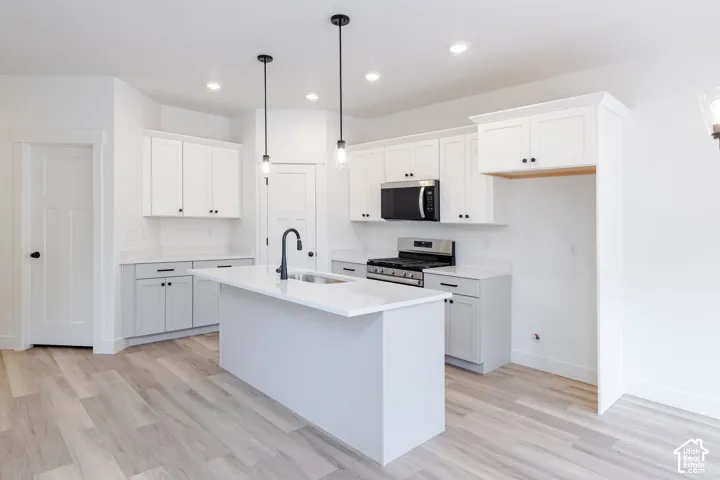 Kitchen featuring two-tone shaker cabinetry, quartz countertops, a central island with an undermount sink and matte black faucet, pendant lighting, and wood-finish flooring
