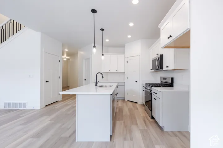 Kitchen featuring an island with a light-toned countertop, custom cabinetry with matte black hardware, recessed lighting, pendant fixtures, and wood-finish flooring