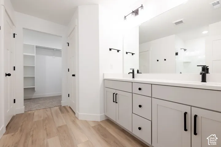 Double vanity with grey shaker-style cabinetry, matte black hardware, dual faucets, and a large wall-to-wall mirror featuring wood-finish flooring