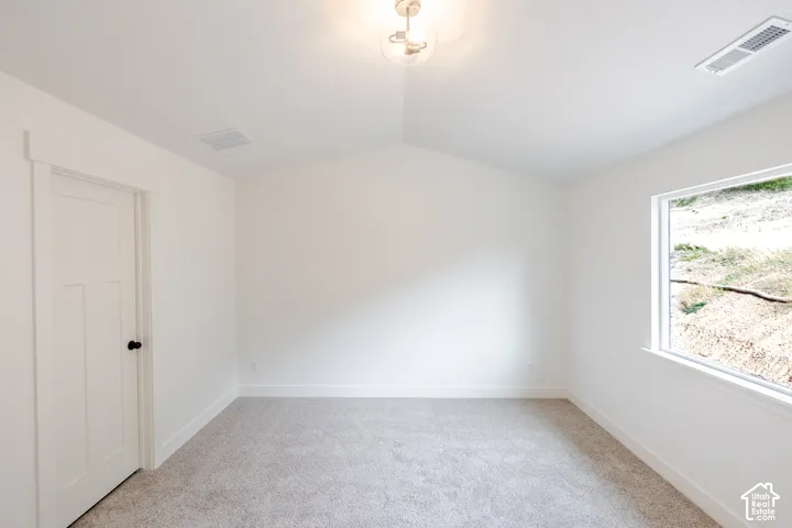 Vaulted ceiling, neutral wall-to-wall carpeting, shaker-style interior door with matte black hardware, and large picture window
