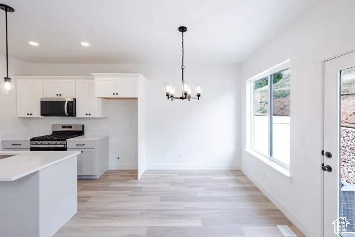 Kitchen featuring white shaker-style cabinetry, a stone-surface island, stainless steel appliances, a multi-light chandelier, and wood-finish flooring