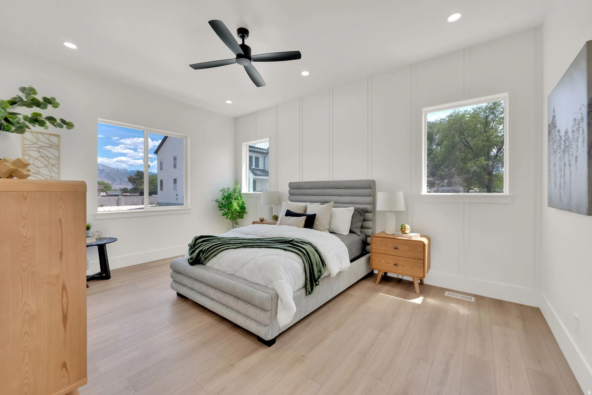 Bright bedroom featuring light wood-finish flooring and multiple windows
