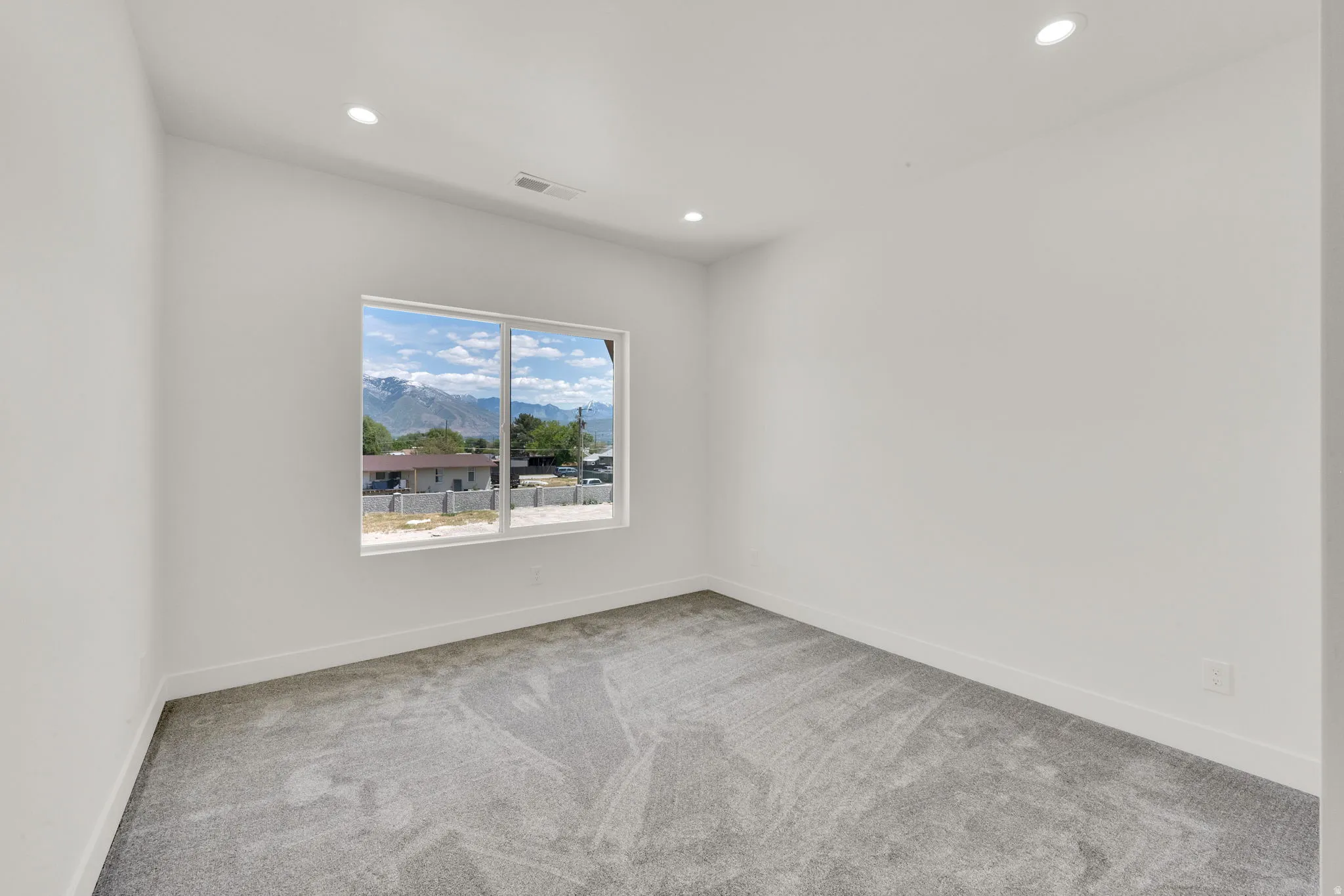 Expansive room featuring a large window, recessed lighting, white walls, and gray patterned carpet