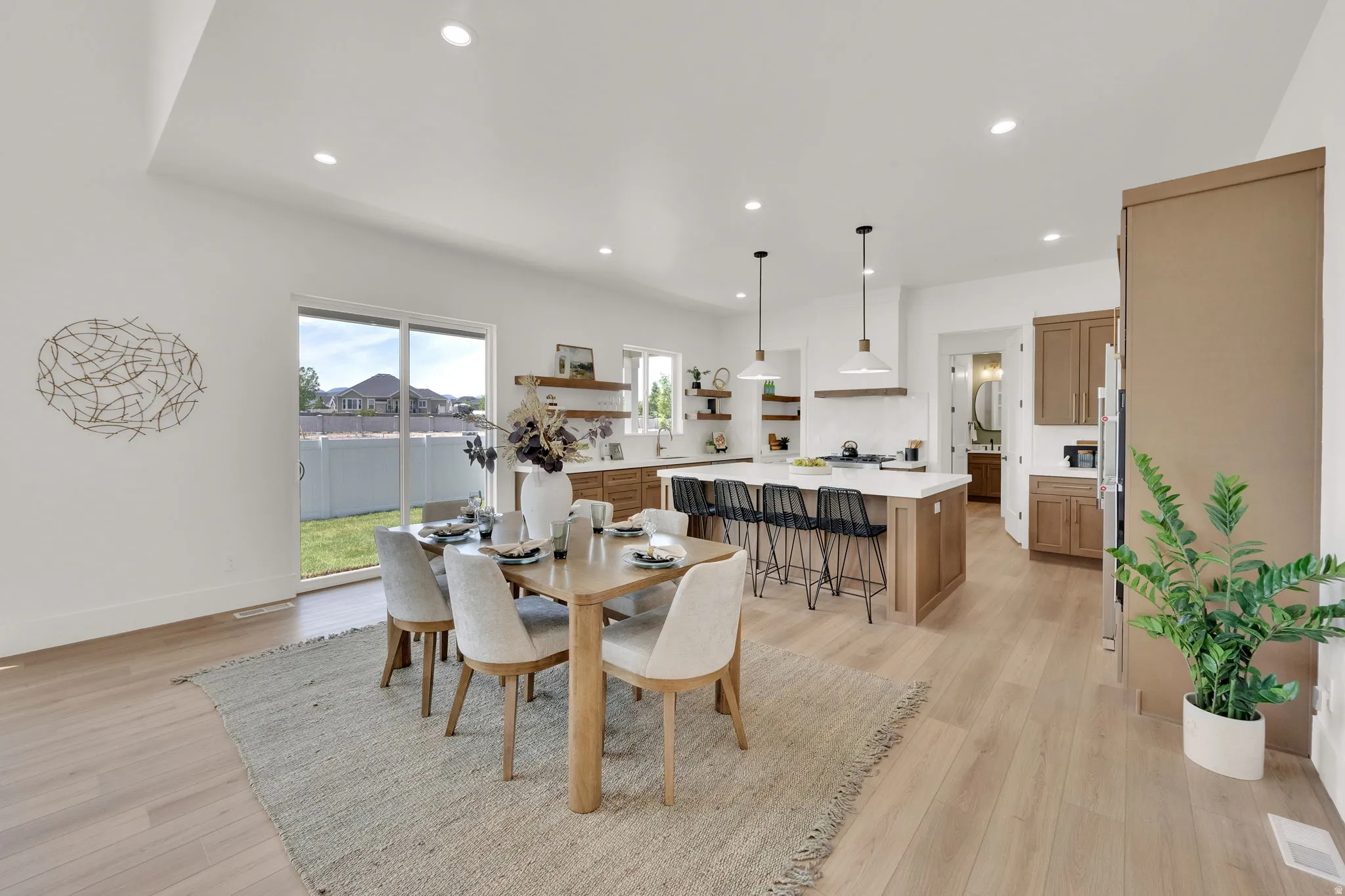 Open-concept living space featuring light wood-finish flooring, recessed lighting, and a sliding glass door to the backyard