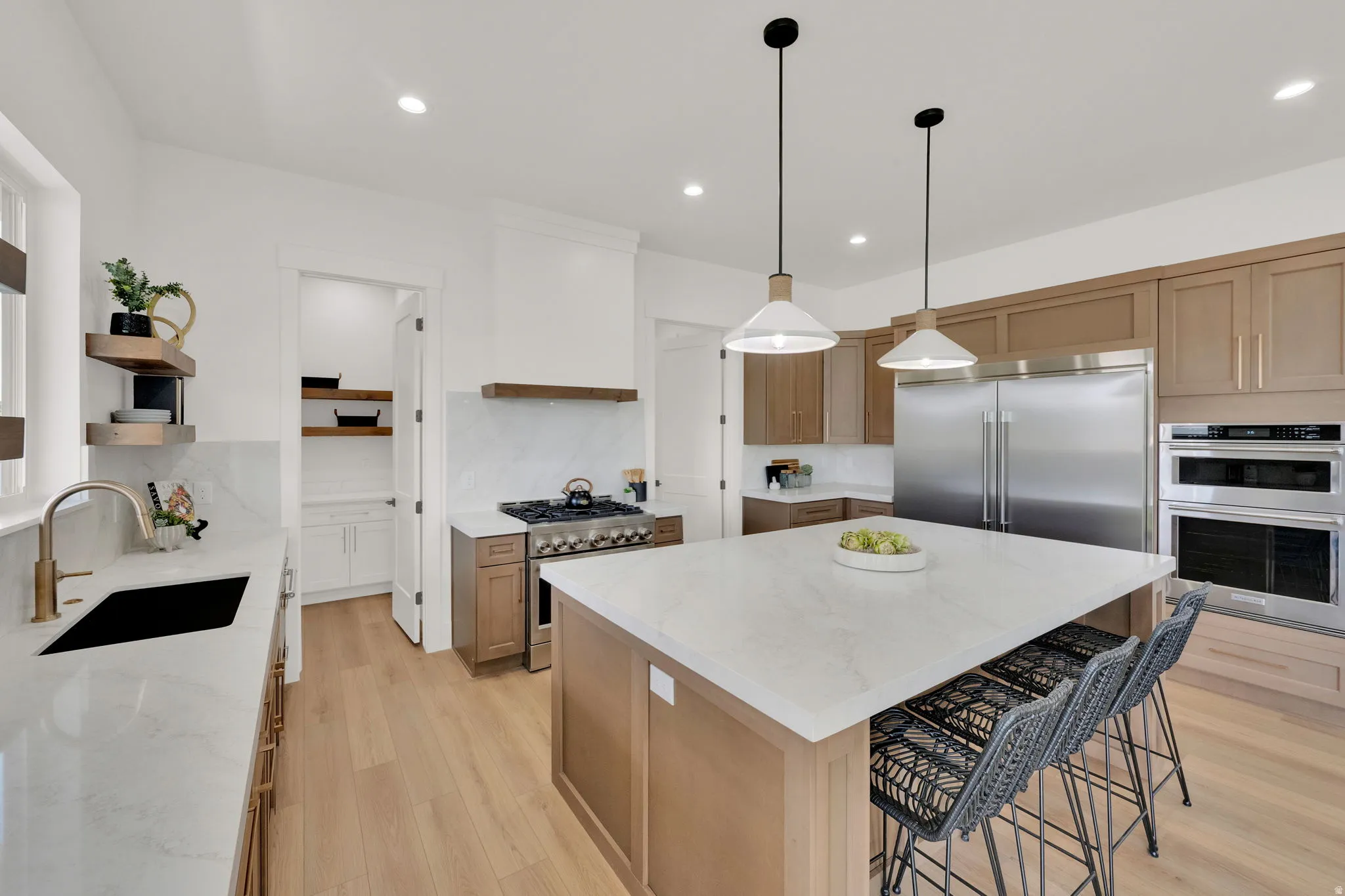 Gourmet kitchen featuring a large central island with seating, stone countertops, light wood-finish flooring, a stainless steel refrigerator, and integrated double ovens