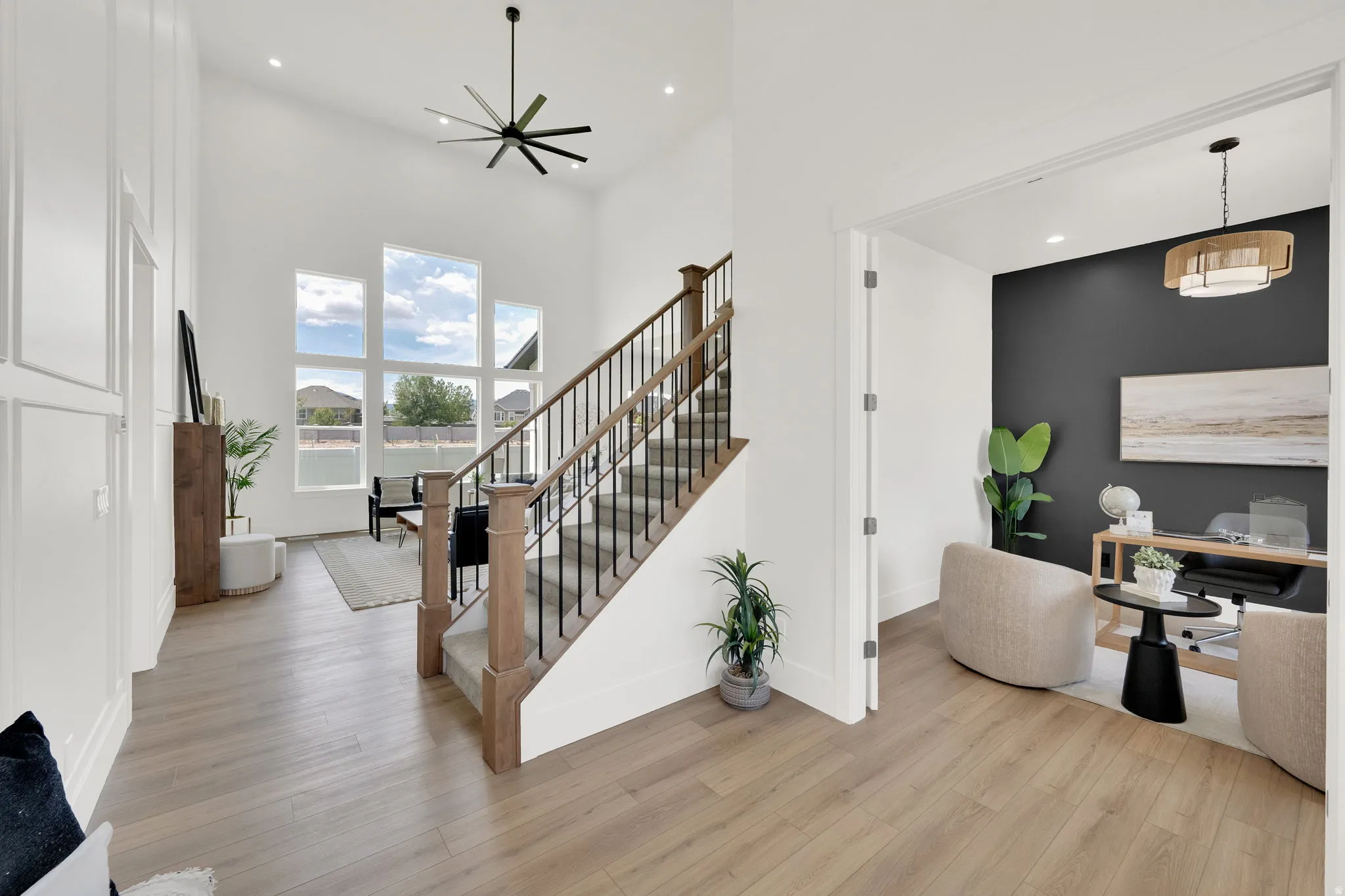 Two-story entry featuring light wood-finish flooring, a contemporary black ceiling fan, and a wood and iron staircase with carpeted treads