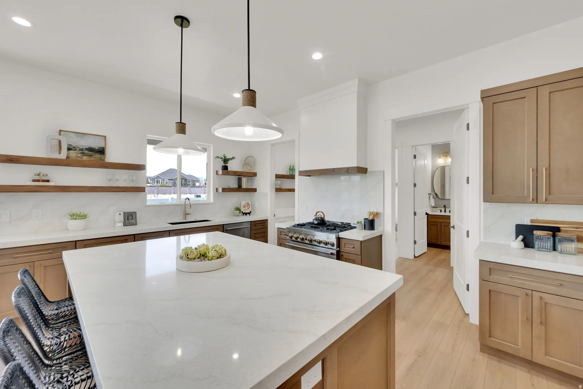 Contemporary kitchen featuring a large central island with a light-toned countertop, wood-finish flooring, recessed lighting, and modern pendant fixtures
