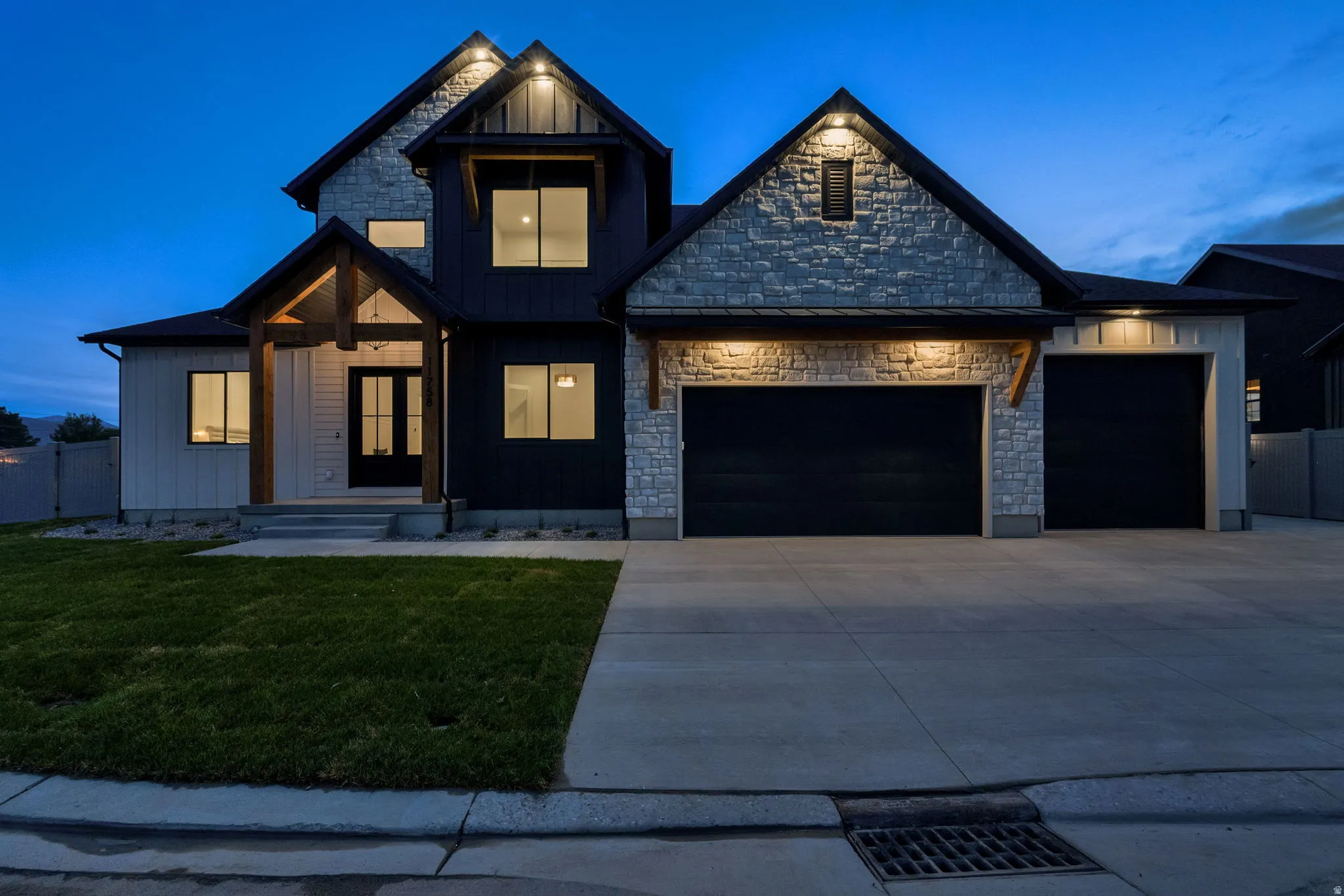 Modern exterior featuring a prominent two-car garage, stone and vertical siding accents, a covered entry with timber beams, a concrete driveway, and a manicured lawn