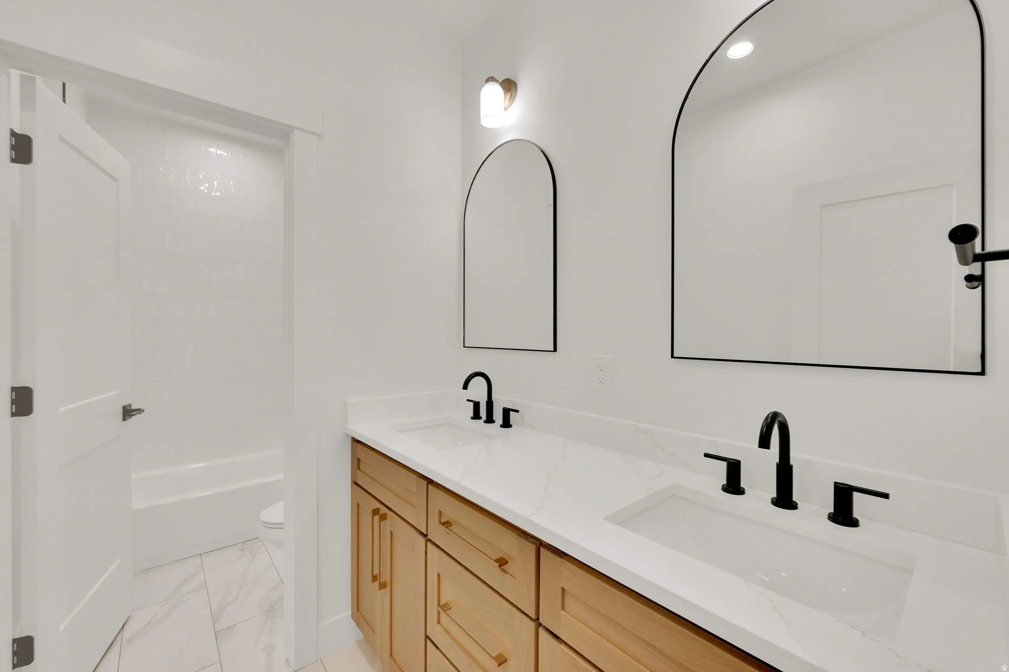 Dual vanity featuring wood-finish cabinetry, integrated sinks, and matte black fixtures