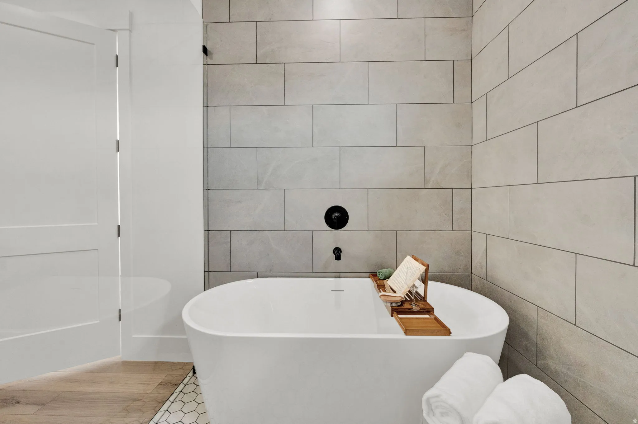 Freestanding soaking tub with matte black fixtures, set against a tiled accent wall