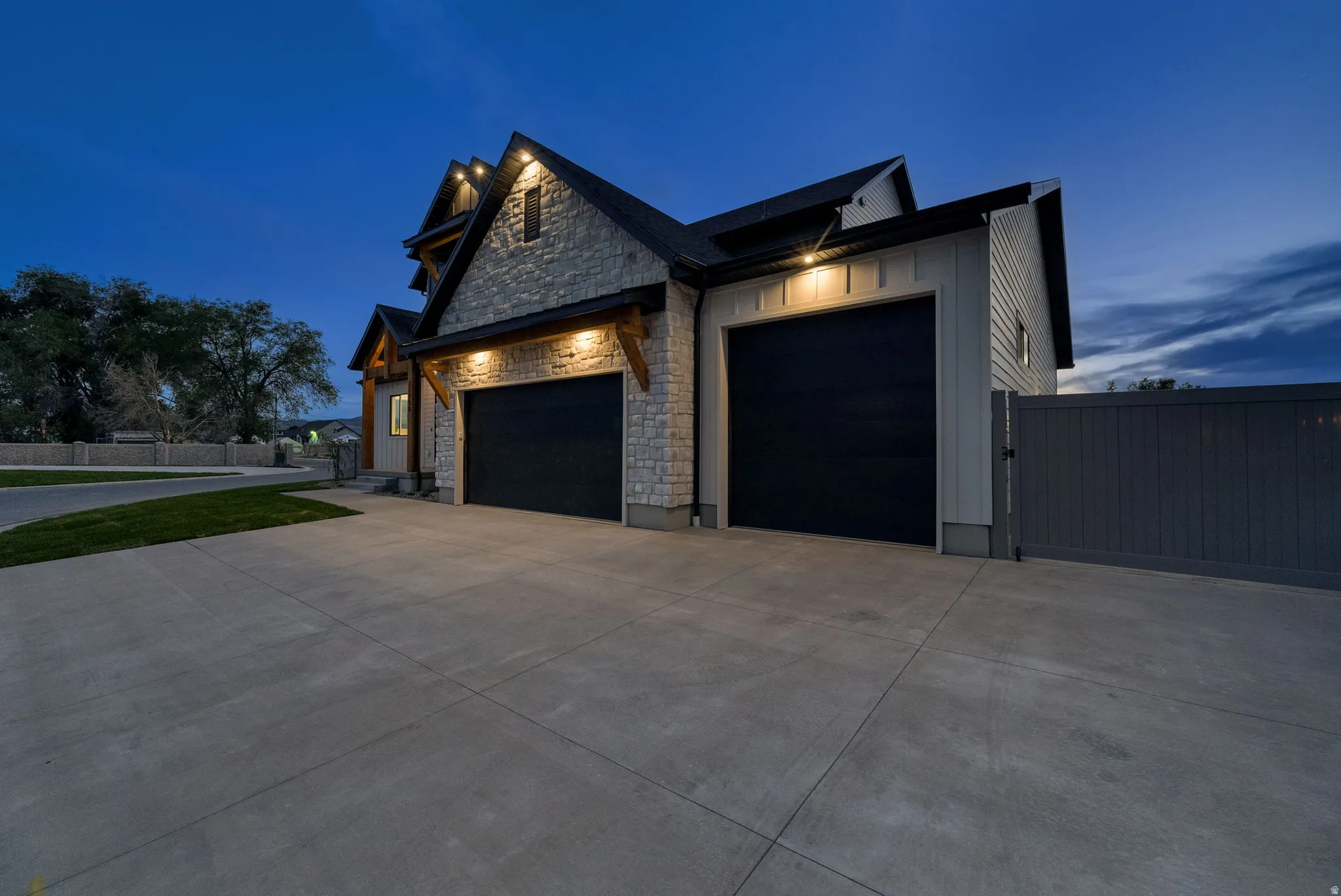 Stone facade residence featuring two garage doors, an expansive concrete driveway, and a privacy fence