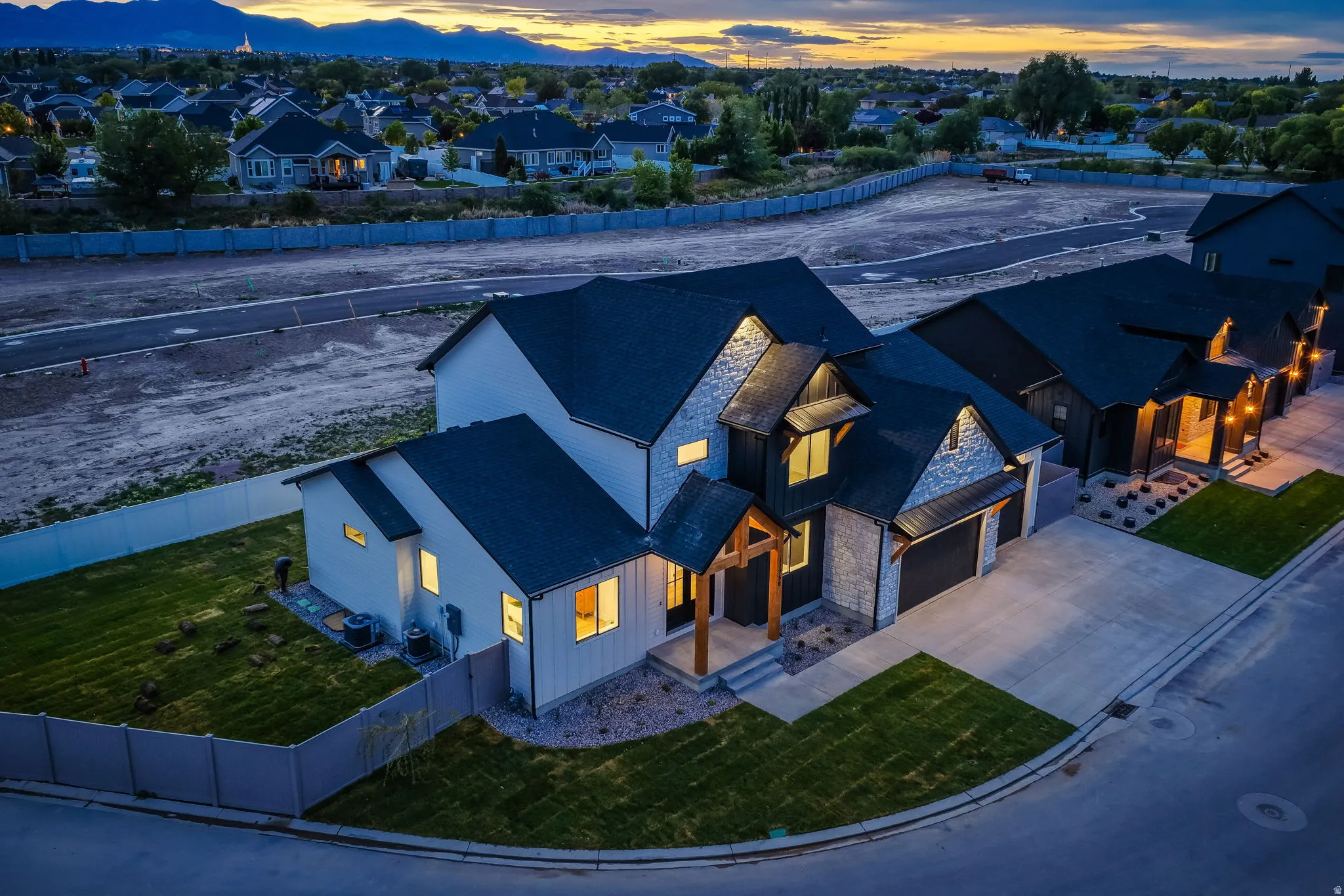 Modern exterior with dark roof and light-toned siding, featuring stone accents, an attached garage, and a covered entry with wood-finish columns