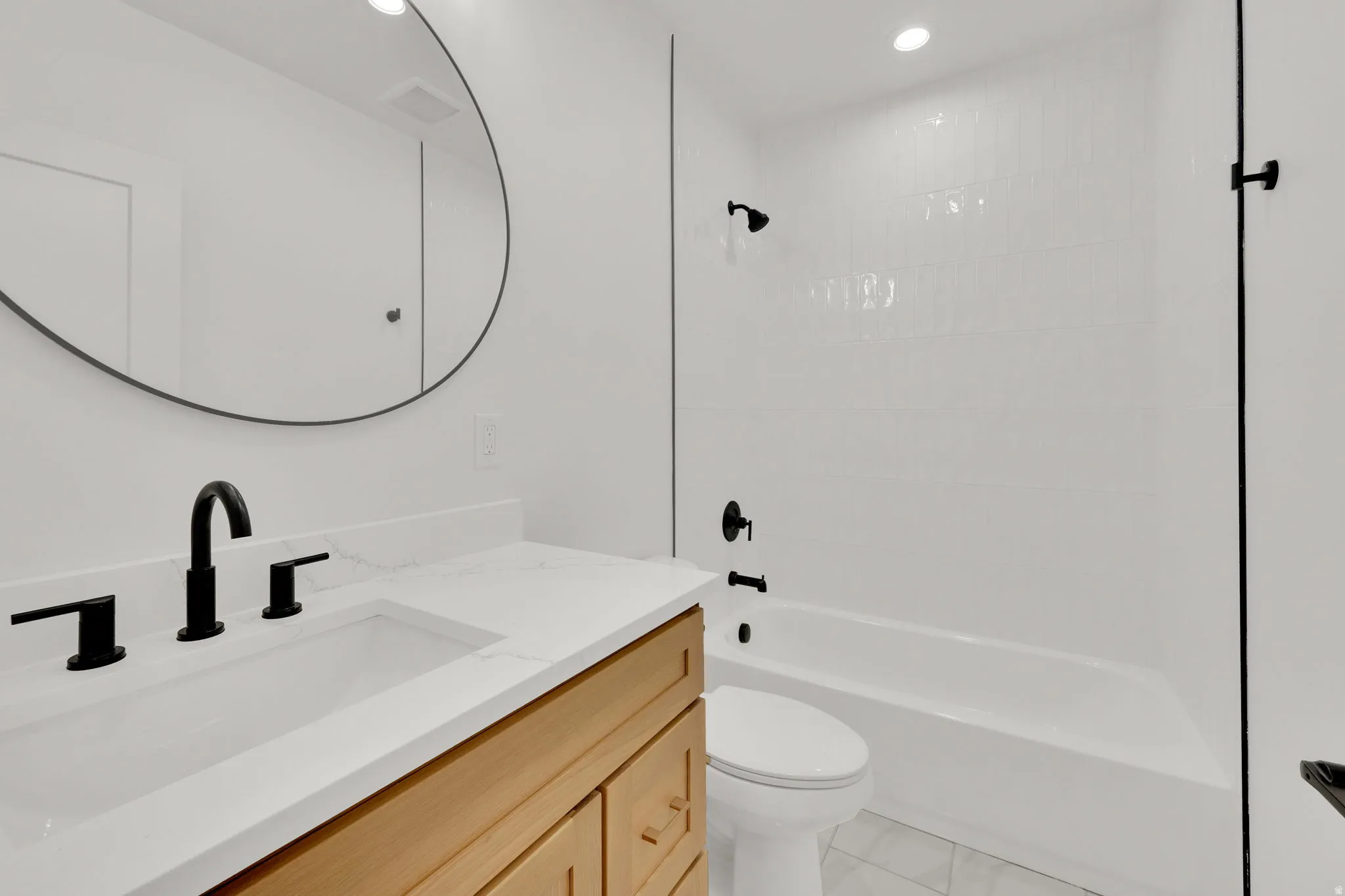 Bathroom featuring a wood-finish vanity with a white countertop and integrated sink, matte black faucet, and a round wall-mounted mirror