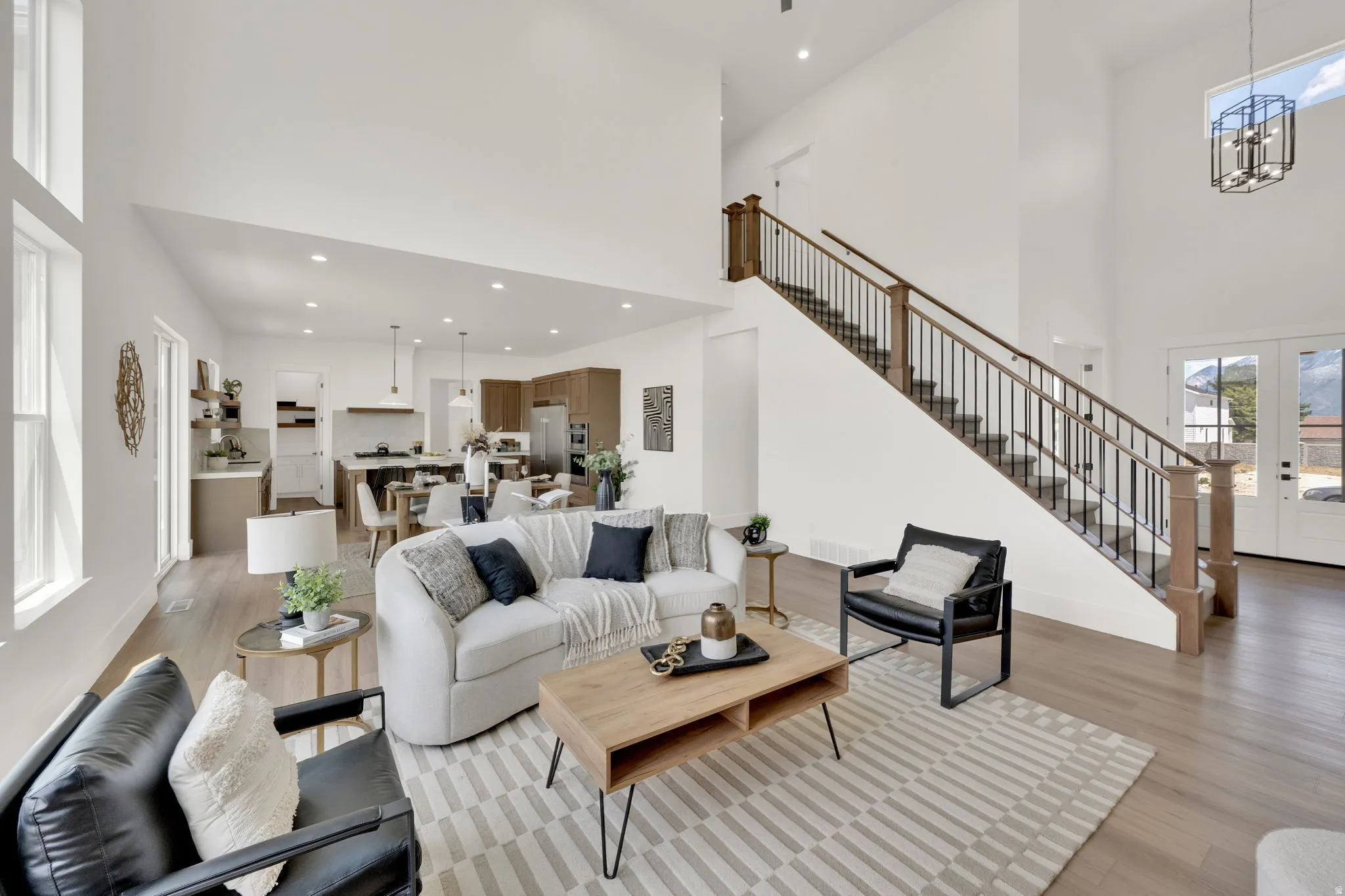 Expansive open-concept living space with vaulted ceilings, wood-finish flooring, and a contemporary staircase featuring wood newel posts and metal balusters