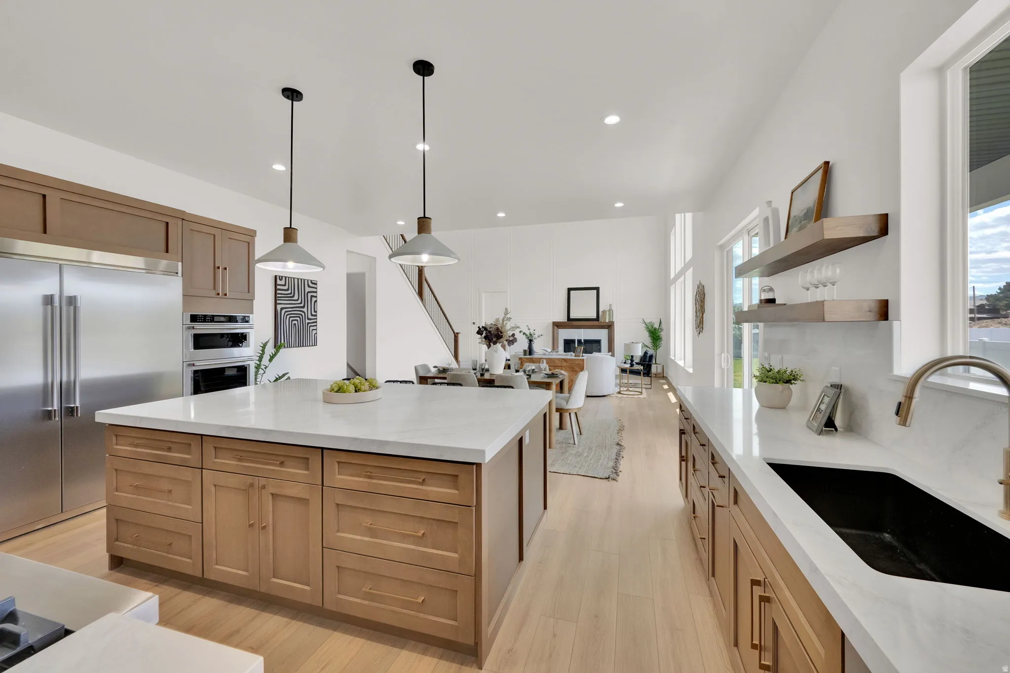 Spacious kitchen featuring natural wood cabinetry, stainless steel appliances, a large center island with pendant lighting, stone countertops, and a built-in kitchen sink with a gooseneck faucet