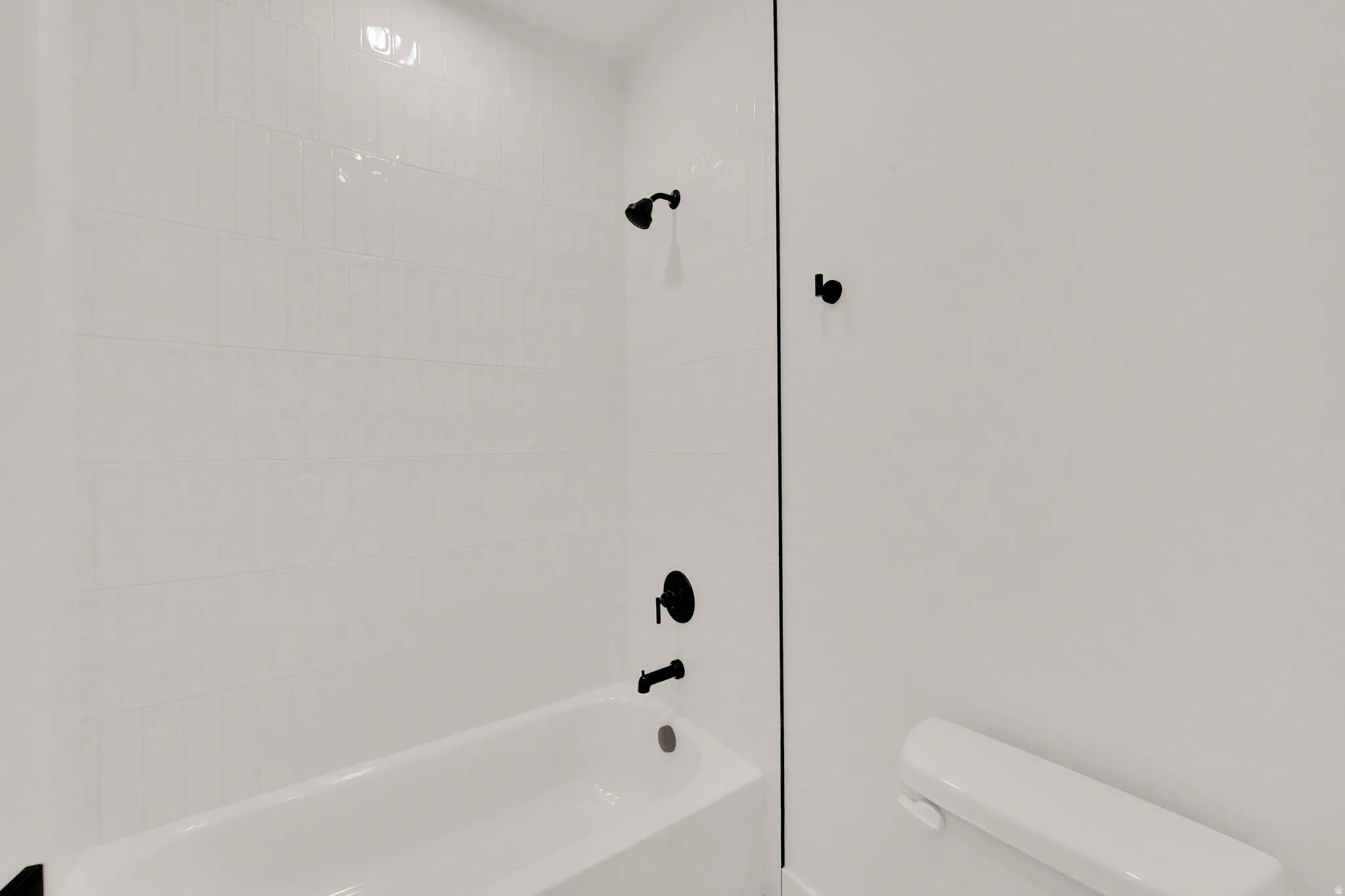 White subway tile shower surround with matte black fixtures and a white bathtub