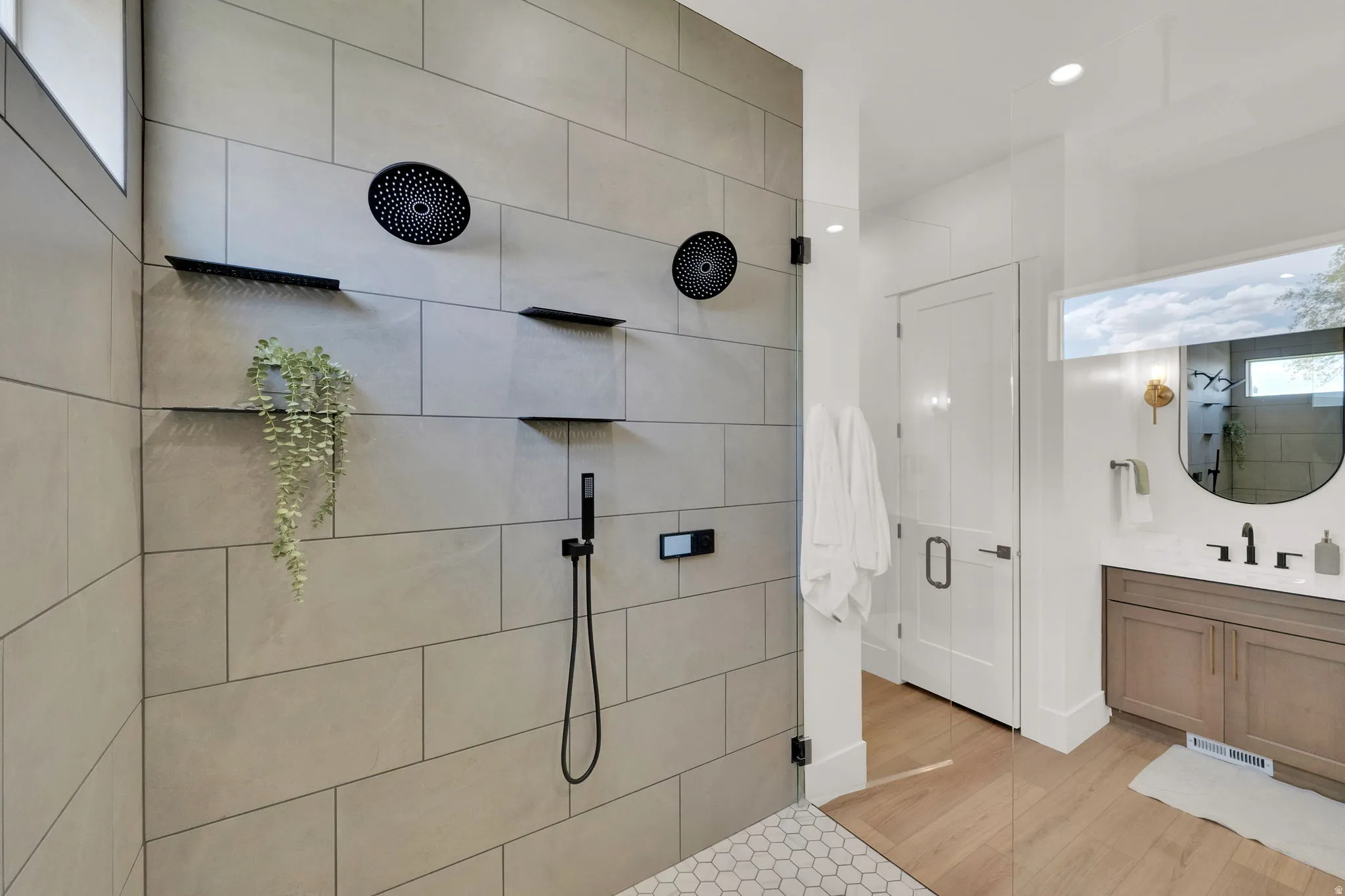 Spacious walk-in shower featuring large format tile, dual rain shower heads, a handheld shower fixture, and multiple built-in shelves