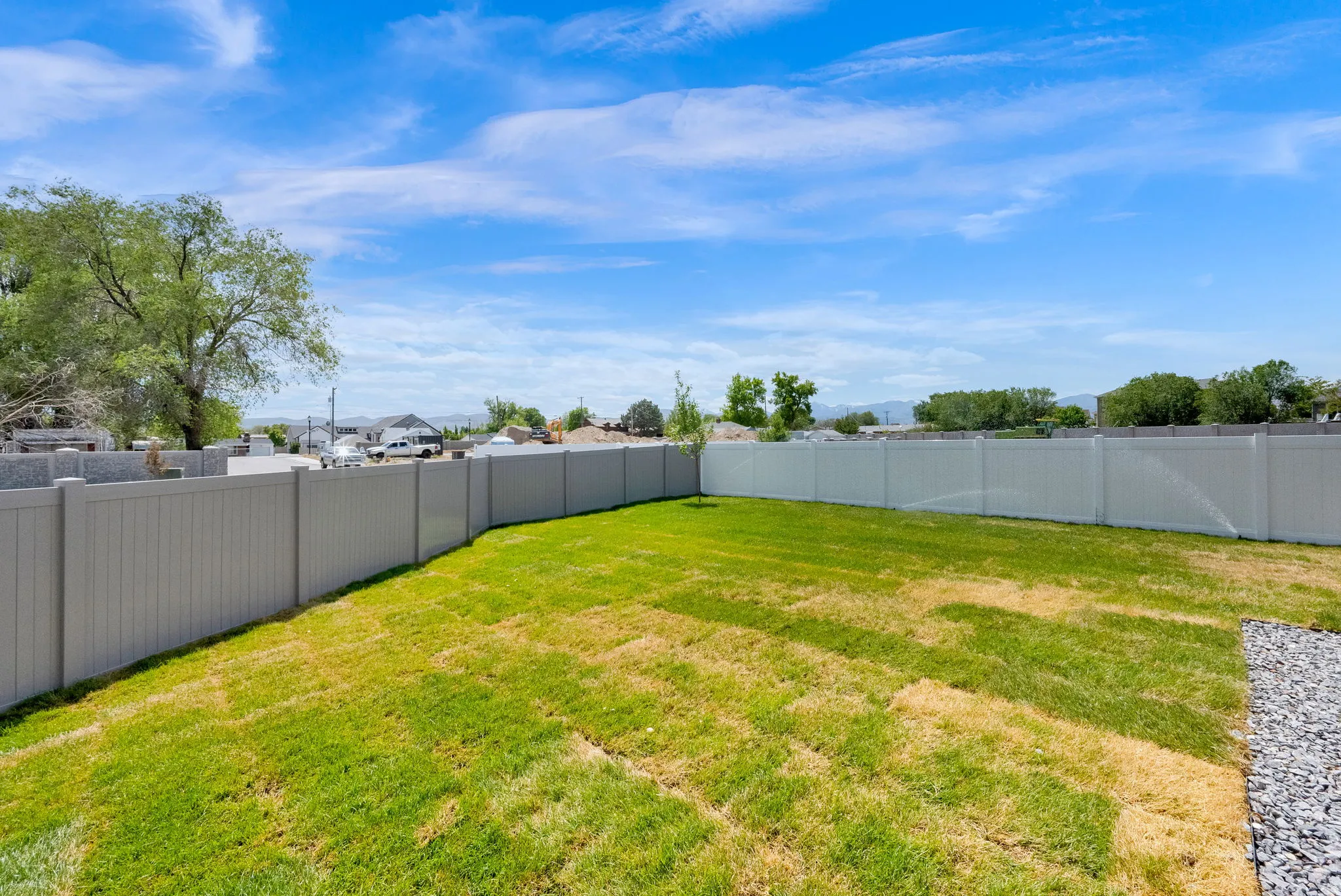 Expansive outdoor space featuring a manicured lawn, full perimeter fencing, and a gravel accent area