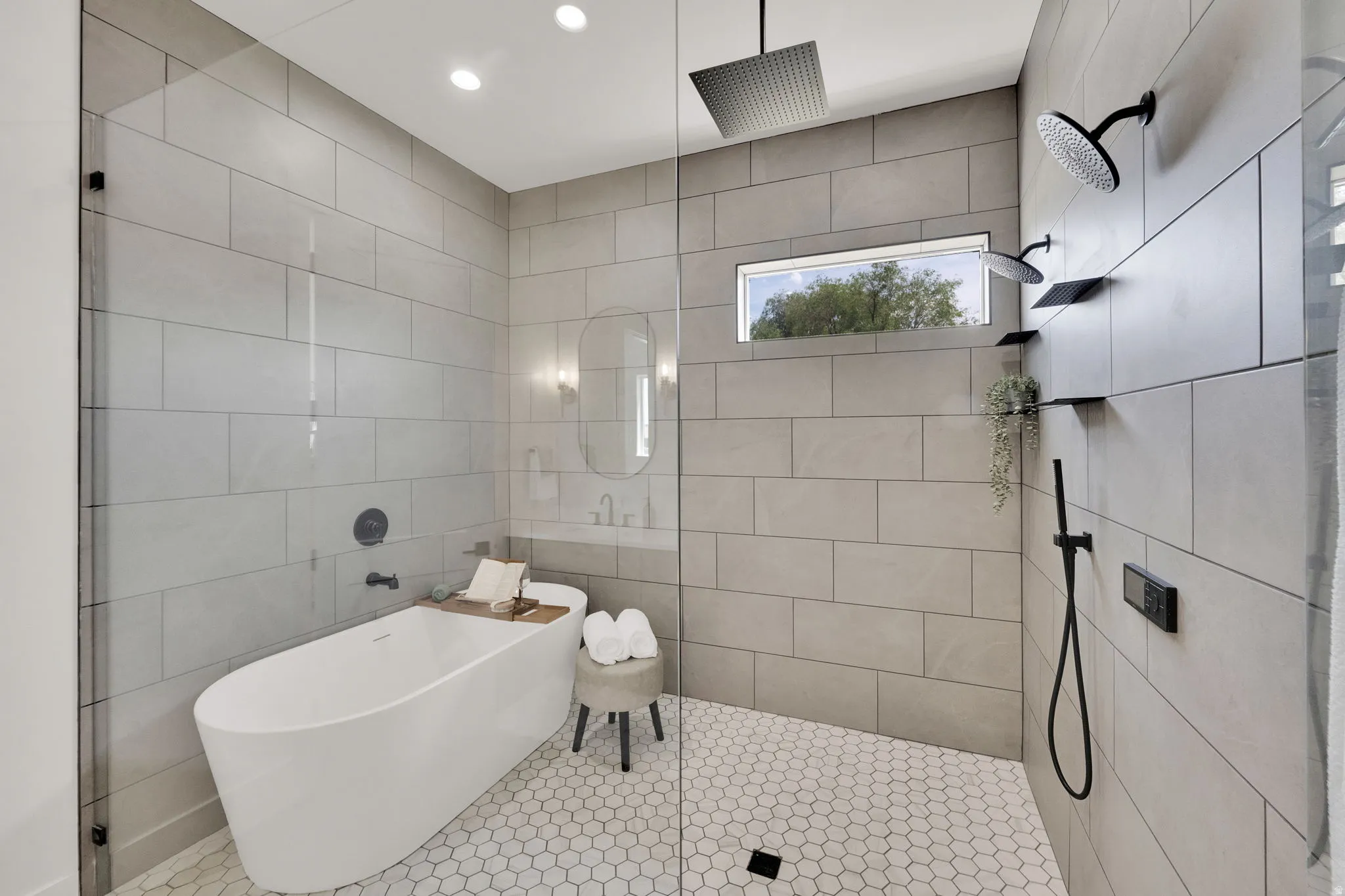 Freestanding soaking tub within a glass-enclosed wet room featuring matte black fixtures, a rain showerhead, a handheld shower, and a horizontal privacy window
