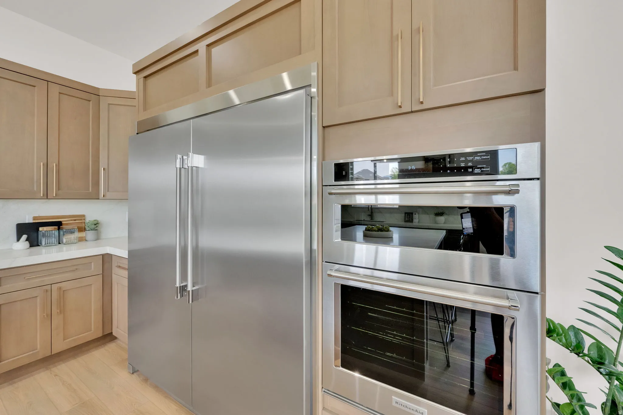 Stainless steel professional-grade refrigerator, integrated double oven, light wood-finish cabinetry, light wood-finish flooring, and white countertop