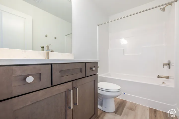 Wood-finish flooring, white vanity countertop, brushed nickel faucet, wood-finish cabinetry, and a white bathtub with shower