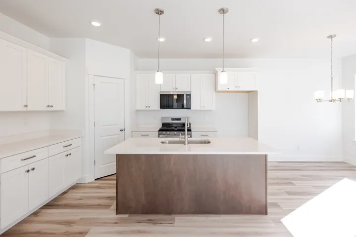 White shaker cabinetry with brushed nickel hardware, light-toned countertops, a stainless steel gas range, and a central island with an undermount sink and pendant lighting
